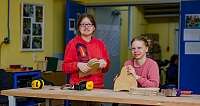 Zwei Frauen arbeiten an Holzprojekten in einer Werkstatt.