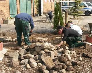 Drei Personen arbeiten im Garten mit Steinen und Erde.
