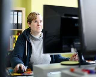 Eine Person sitzt an einem Schreibtisch und arbeitet am Computer.